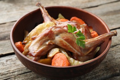 Tasty cooked rabbit with vegetables in bowl on wooden table, closeup