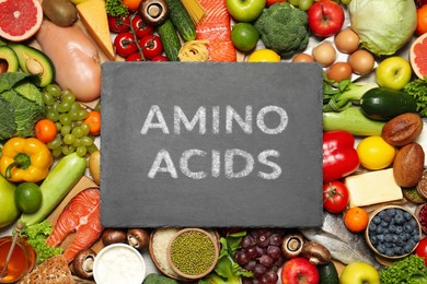 Image of Different organic products and slate board with text AMINO ACIDS, top view 