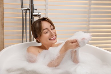 Photo of Happy woman taking bath with foam in tub indoors