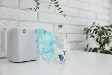 Photo of Modern nebulizer with face mask and medicines on white table near brick wall. Equipment for inhalation