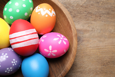 Photo of Colorful Easter eggs in bowl on wooden background, top view. Space for text