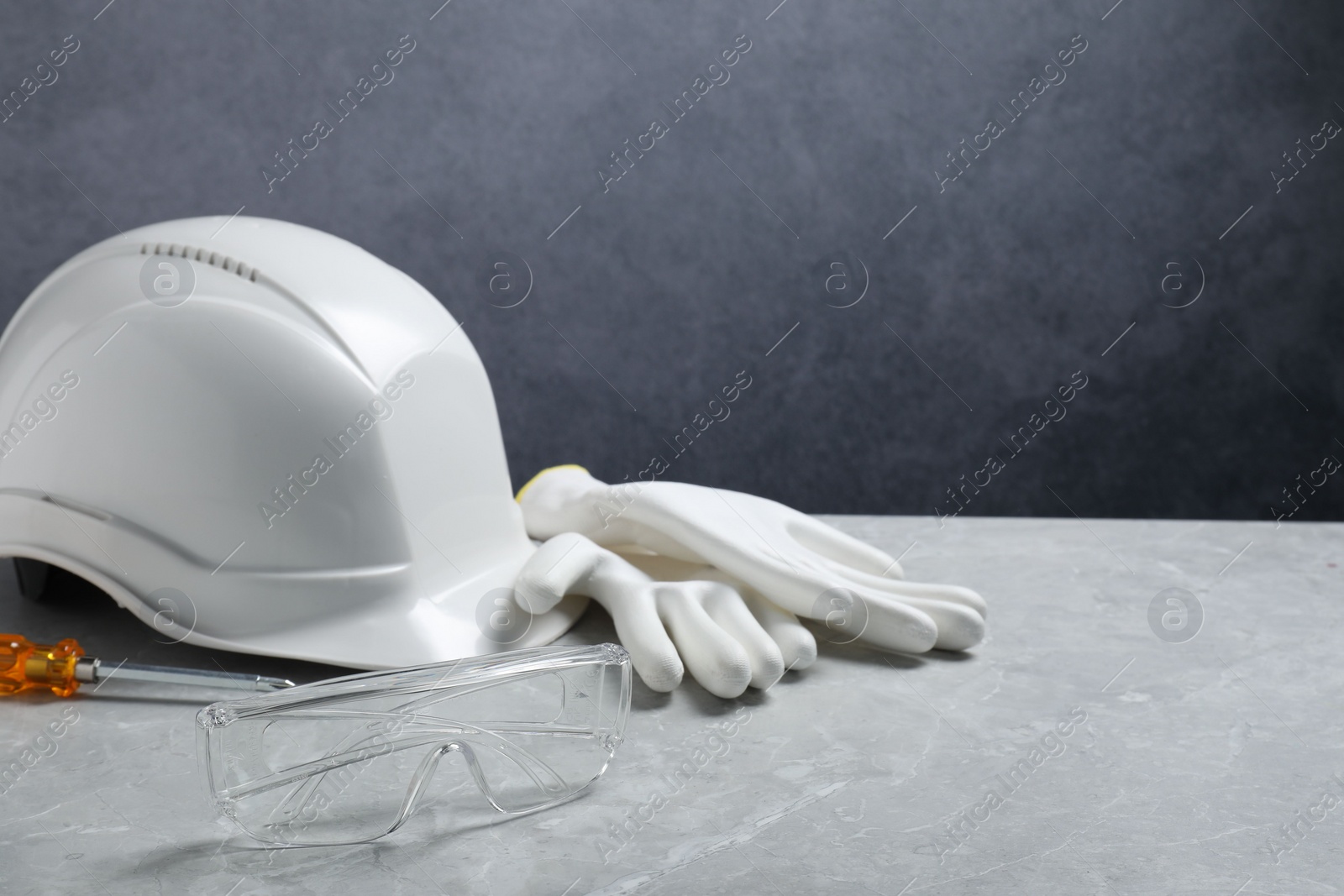 Photo of Hard hat, protective gloves, goggles and screwdriver on grey surface. Space for text