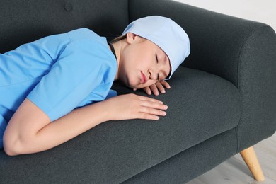 Tired young doctor sleeping on sofa indoors