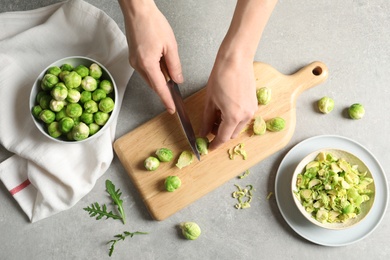 Photo of Woman cutting fresh Brussels sprouts on wooden board, top view