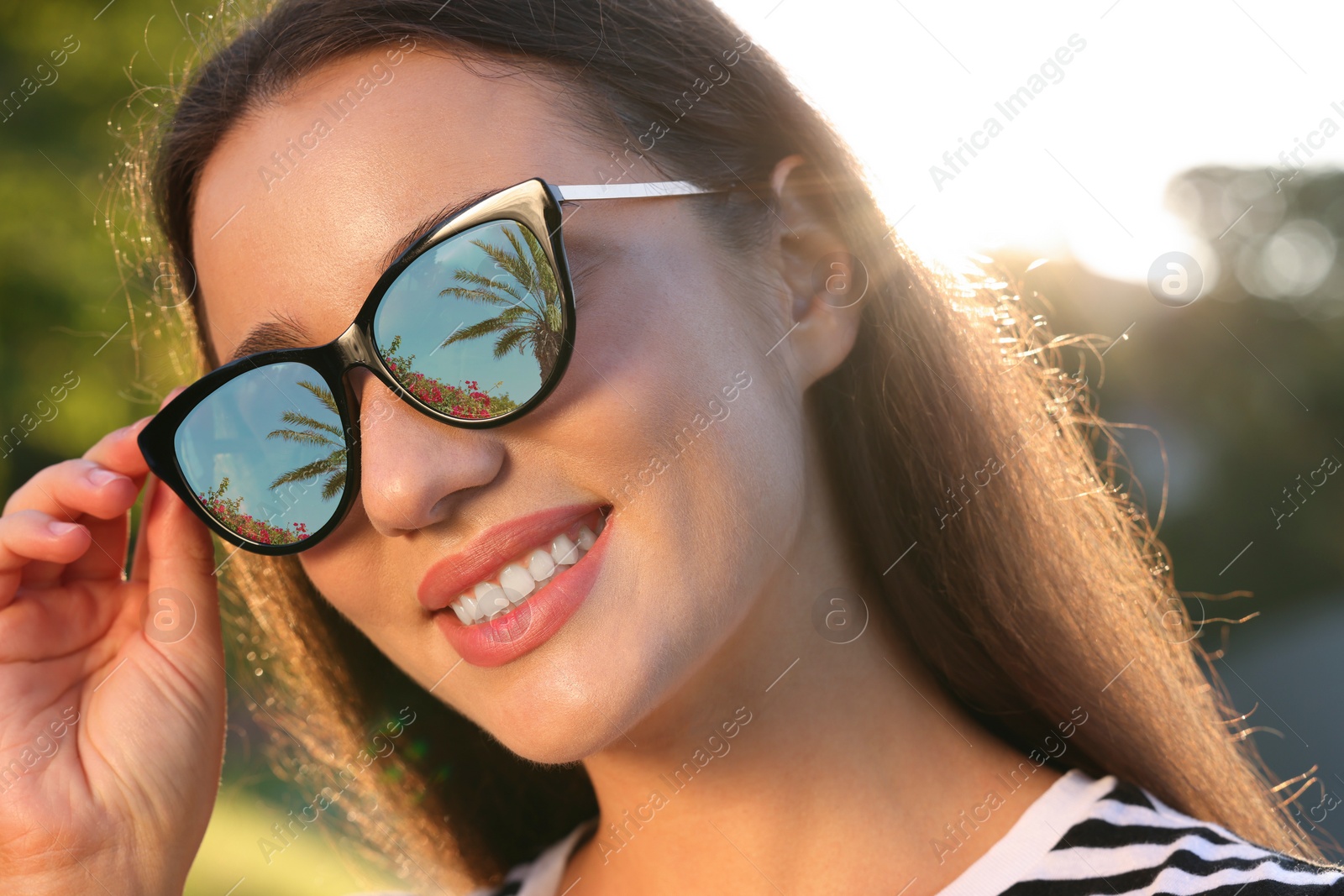 Image of Beautiful woman in sunglasses on sunny day outdoors. Palm tree, flowers and sky reflecting in lenses