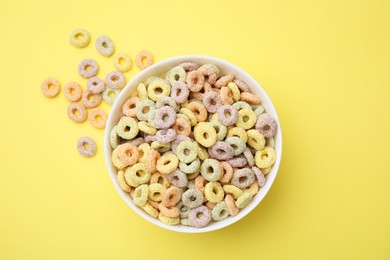 Photo of Tasty cereal rings in bowl on yellow table, top view