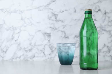 Photo of Glass and bottle with water on table against white marble background, space for text