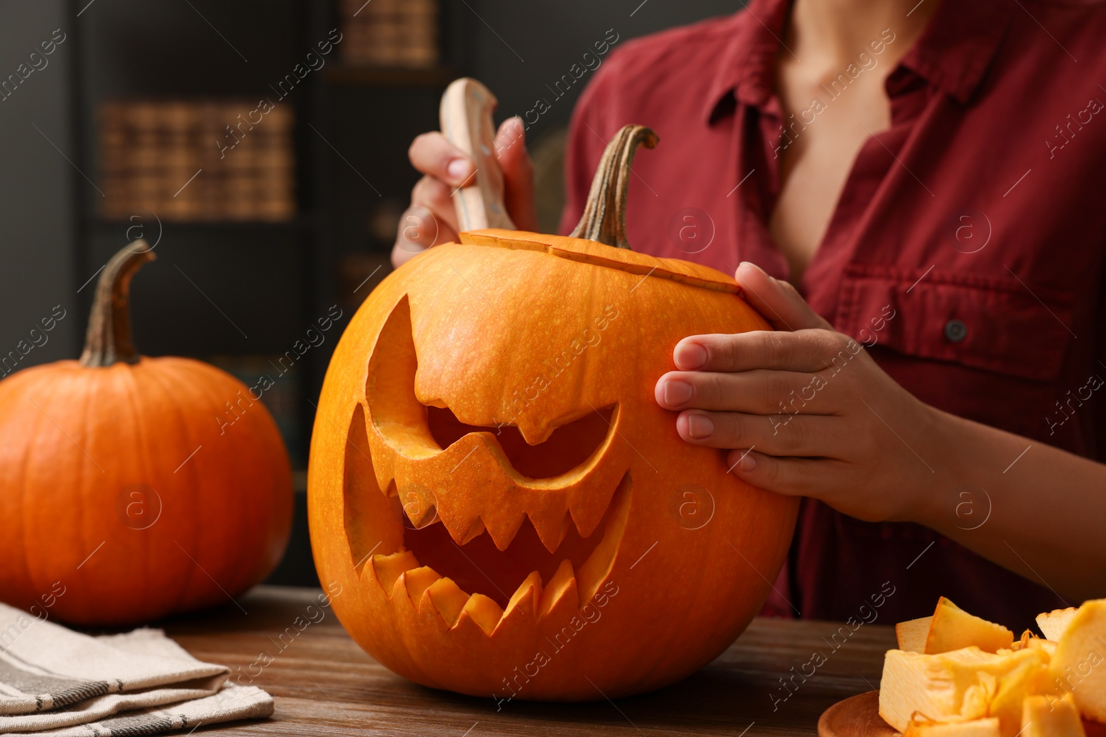 Photo of Woman carving pumpkin for Halloween at wooden table indoors, closeup