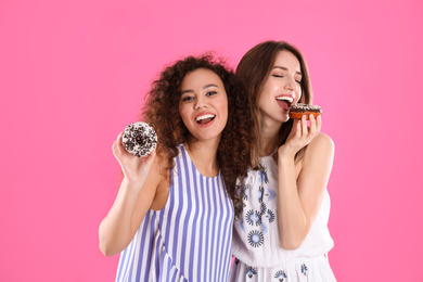 Beautiful young women with donuts on pink background