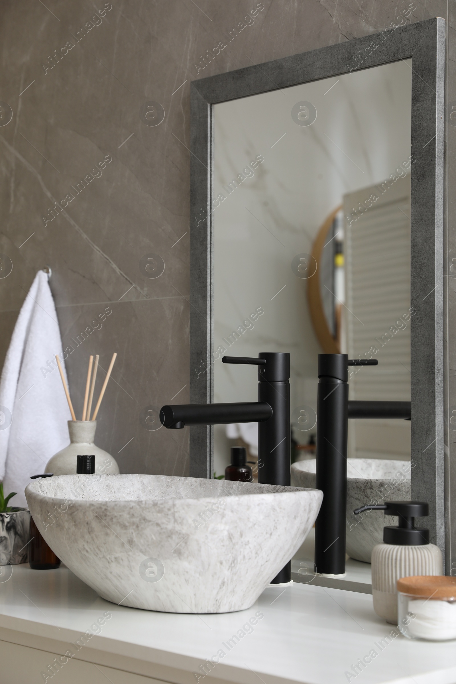 Photo of Stone vessel sink with faucet and toiletries on white countertop in bathroom