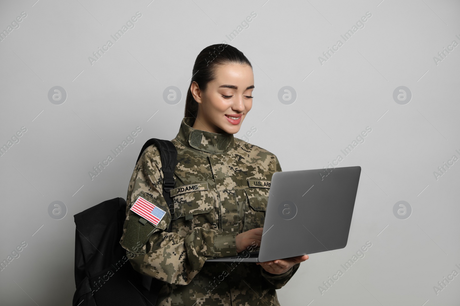 Photo of Female soldier with laptop and backpack on light grey background. Military education