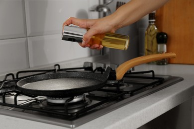 Photo of Woman spraying cooking oil onto frying pan in kitchen, closeup