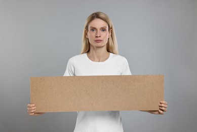 Woman holding blank cardboard banner on grey background, space for text