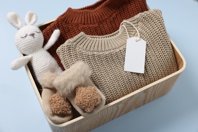 Different baby accessories, knitted sweaters and blank card in box on light blue background