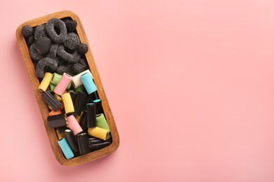 Photo of Wooden container of tasty liquorice candies on pink background, top view. Space for text