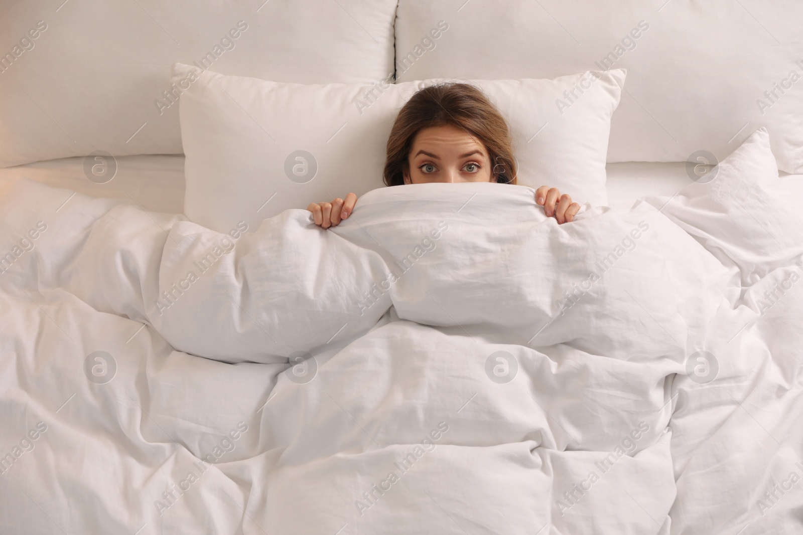 Photo of Woman hiding under warm white blanket in bed, above view