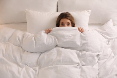 Woman hiding under warm white blanket in bed, above view