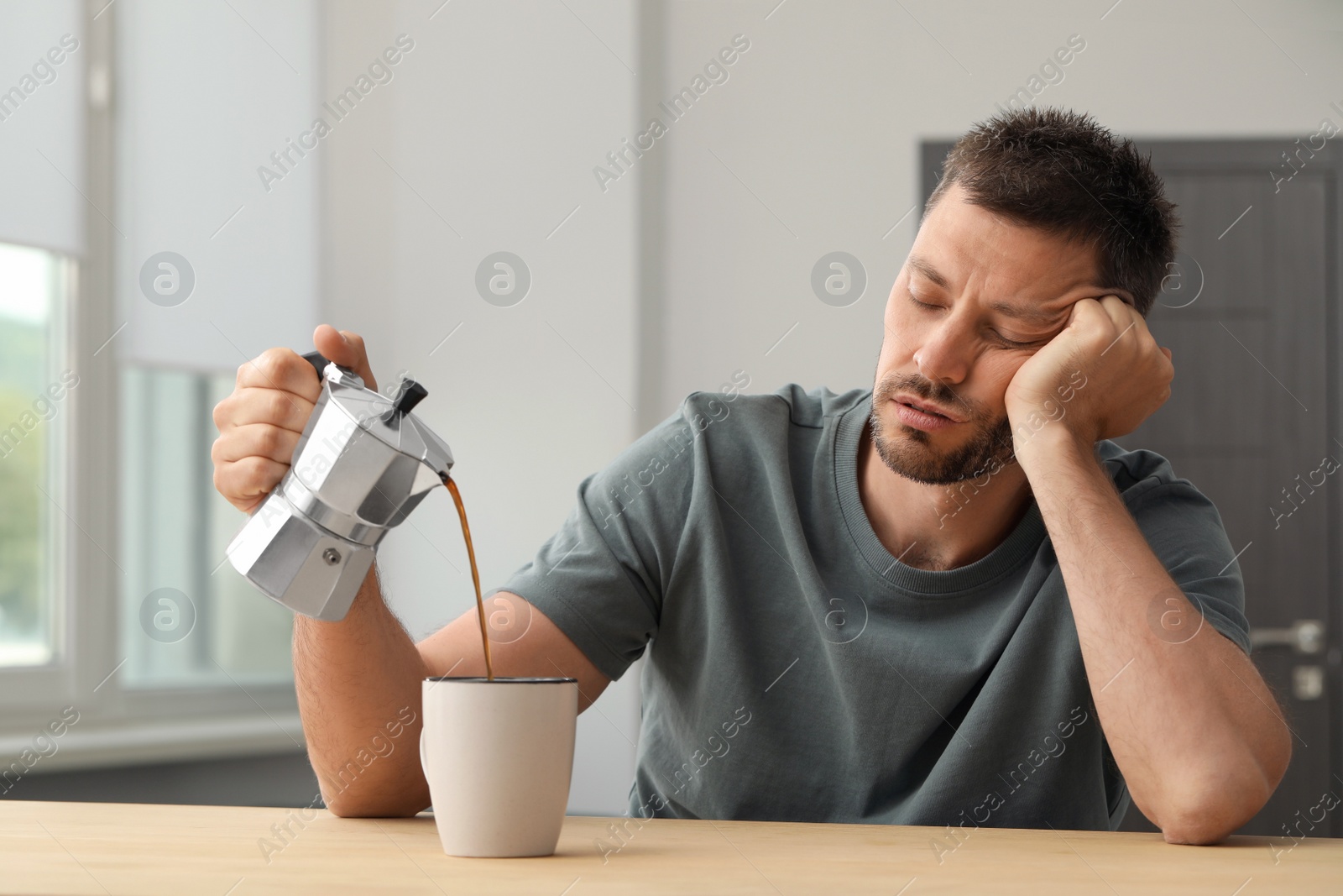 Photo of Sleepy man pouring coffee in cup at wooden table indoors