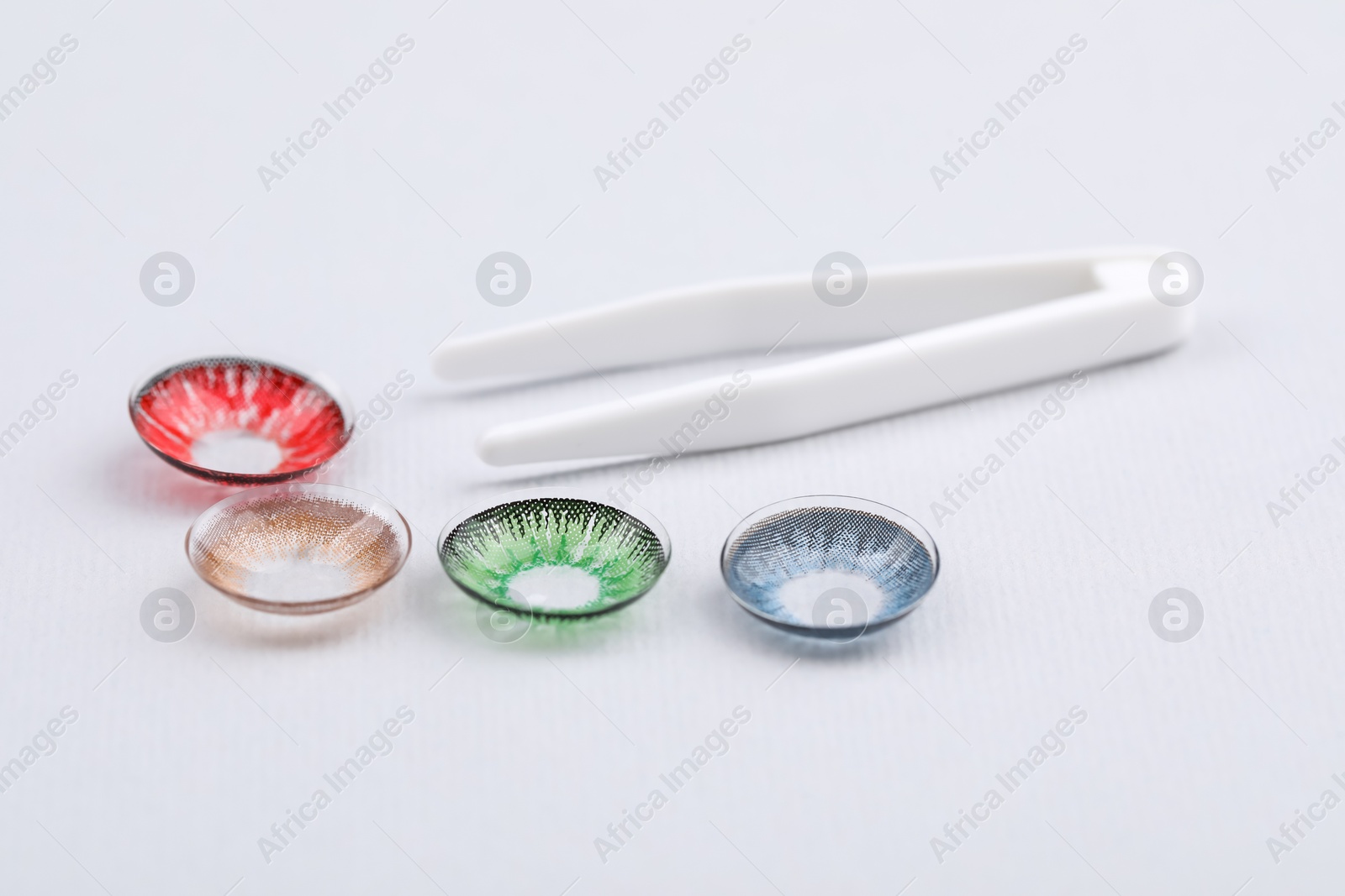 Photo of Different color contact lenses and tweezers on white background