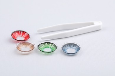 Photo of Different color contact lenses and tweezers on white background
