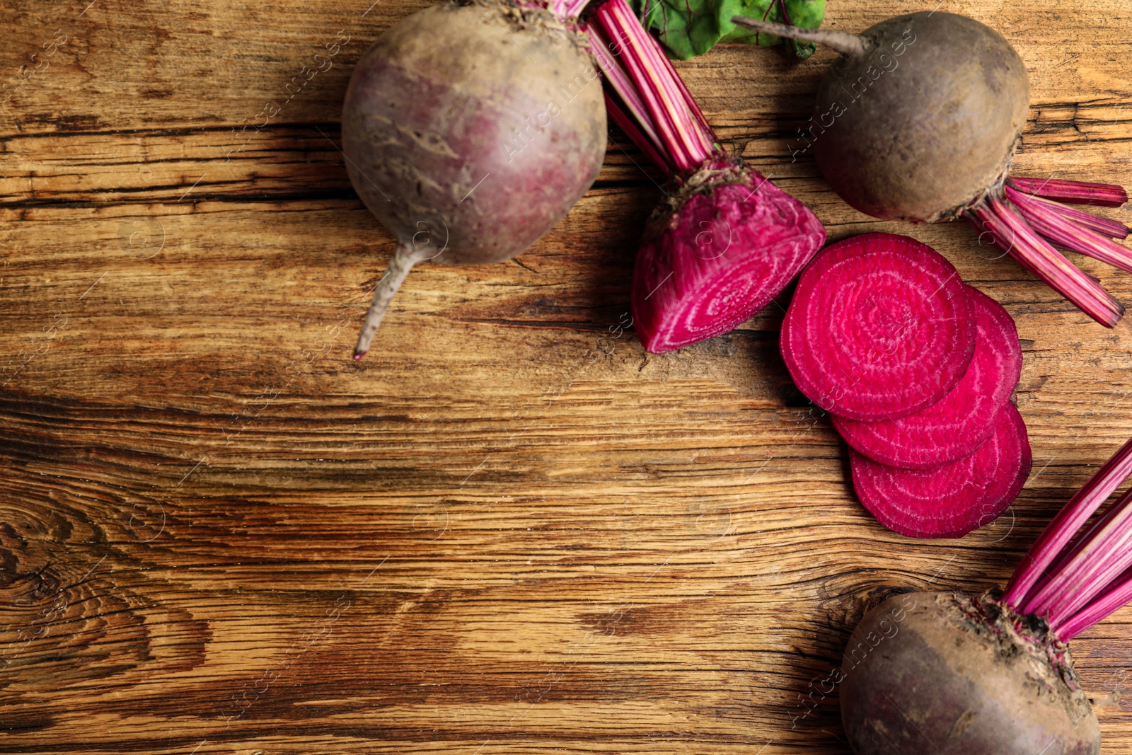 Photo of Cut and whole raw beets on wooden table, flat lay. Space for text