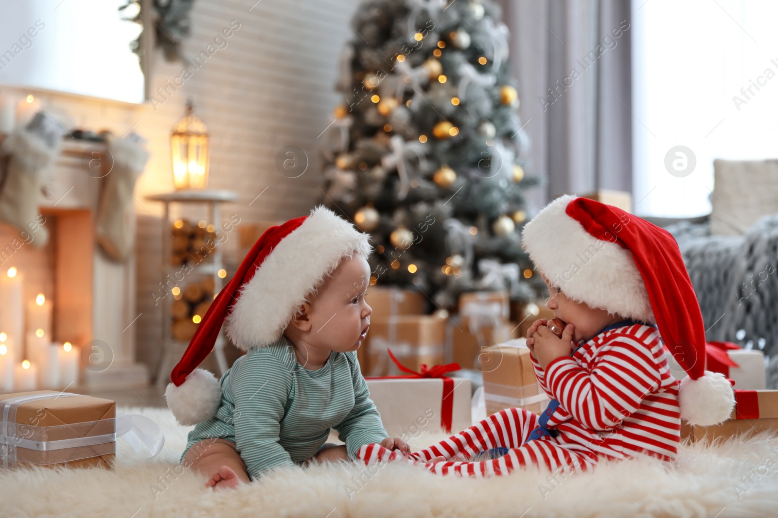 Image of Cute children in Santa hats on floor in room with Christmas tree