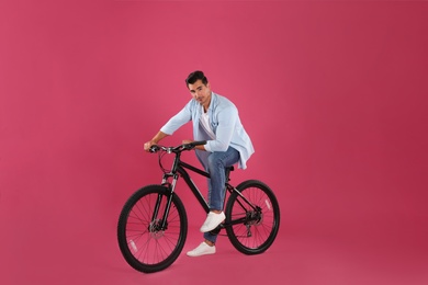 Handsome young man with modern bicycle on pink background