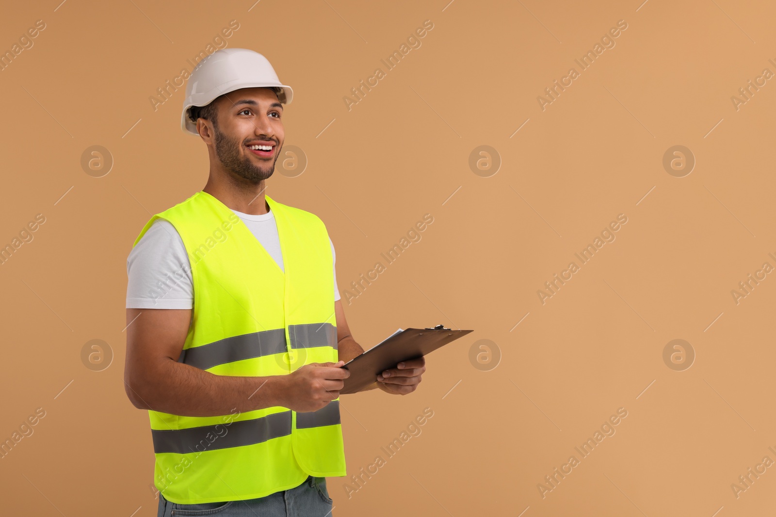 Photo of Engineer in hard hat holding clipboard on beige background, space for text