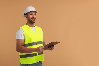 Photo of Engineer in hard hat holding clipboard on beige background, space for text