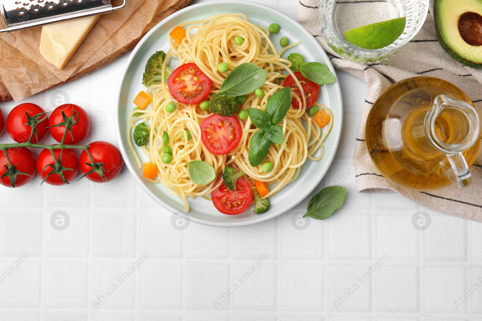 Photo of Plate of delicious pasta primavera and ingredients on white tiled table, flat lay