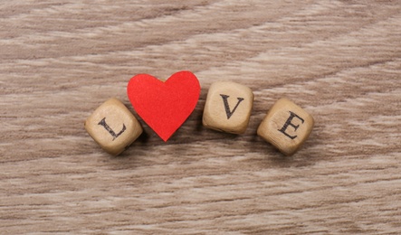 Mini cubes with letters and red paper heart forming word Love on wooden background, flat lay