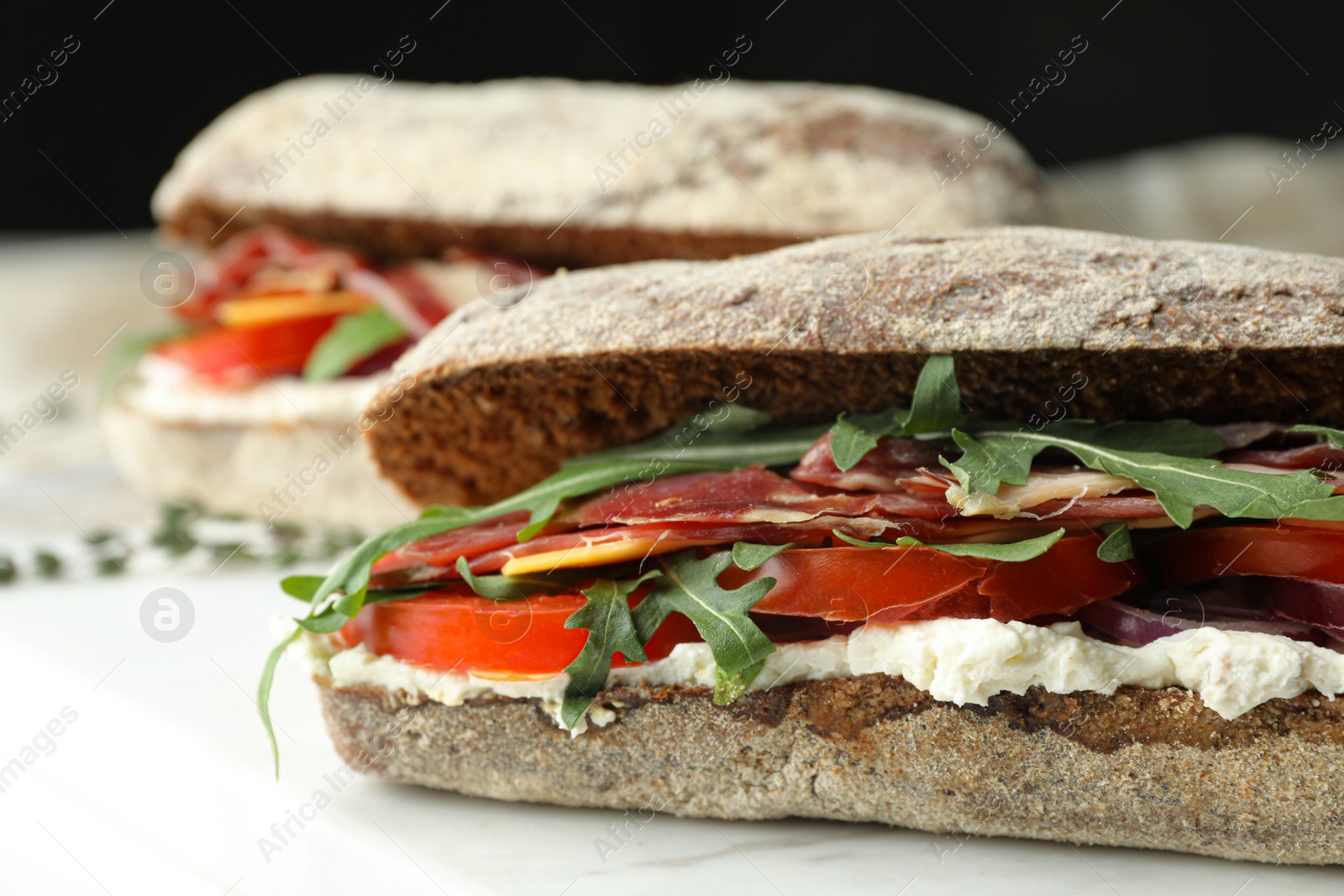 Photo of Delicious sandwiches with fresh vegetables and prosciutto on white table, closeup