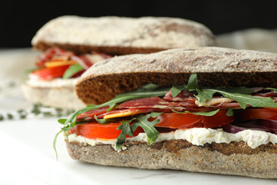 Photo of Delicious sandwiches with fresh vegetables and prosciutto on white table, closeup