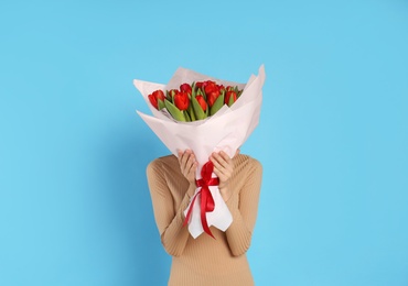 Photo of Woman with red tulip bouquet on light blue background. 8th of March celebration