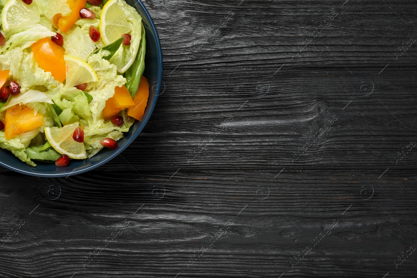 Photo of Delicious salad with Chinese cabbage, lemon, persimmon and pomegranate seeds on black wooden table, top view. Space for text