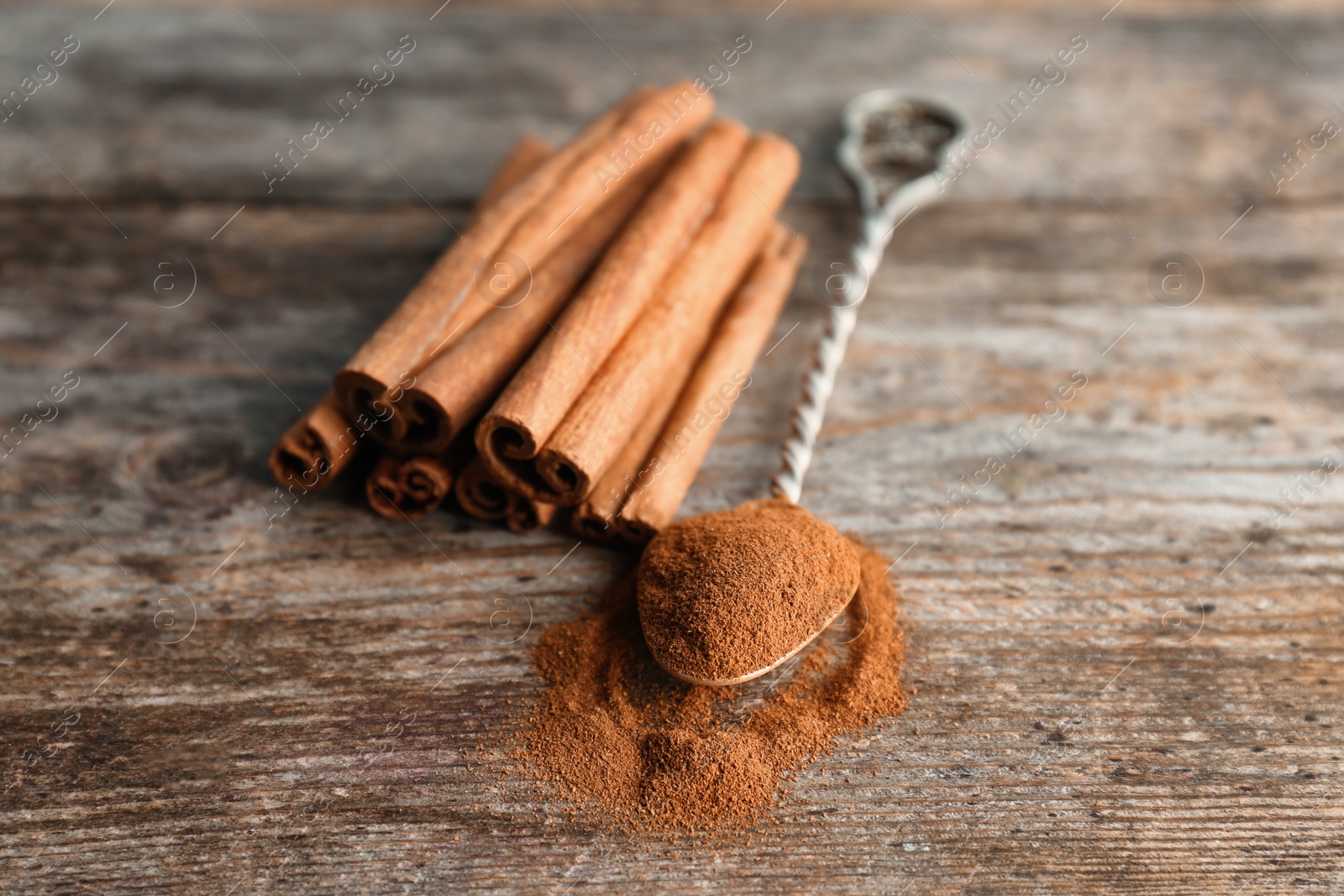 Photo of Spoon with aromatic cinnamon powder and sticks on wooden background