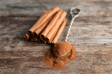 Photo of Spoon with aromatic cinnamon powder and sticks on wooden background