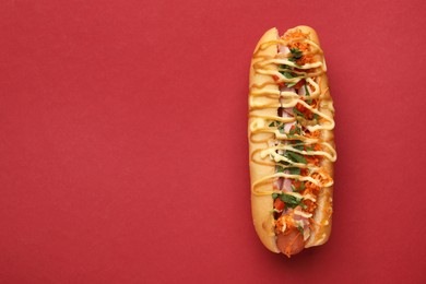 Photo of Delicious hot dog with bacon, carrot and parsley on red background, top view. Space for text