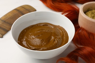Photo of Bowl of henna cream and red strand on white table, closeup. Natural hair coloring