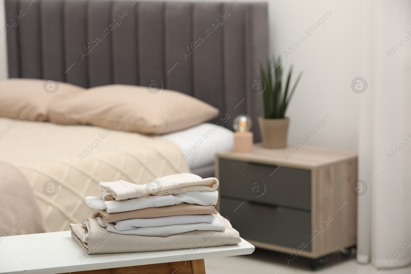 Photo of Stack of different folded clothes on bedside bench indoors, closeup. Space for text