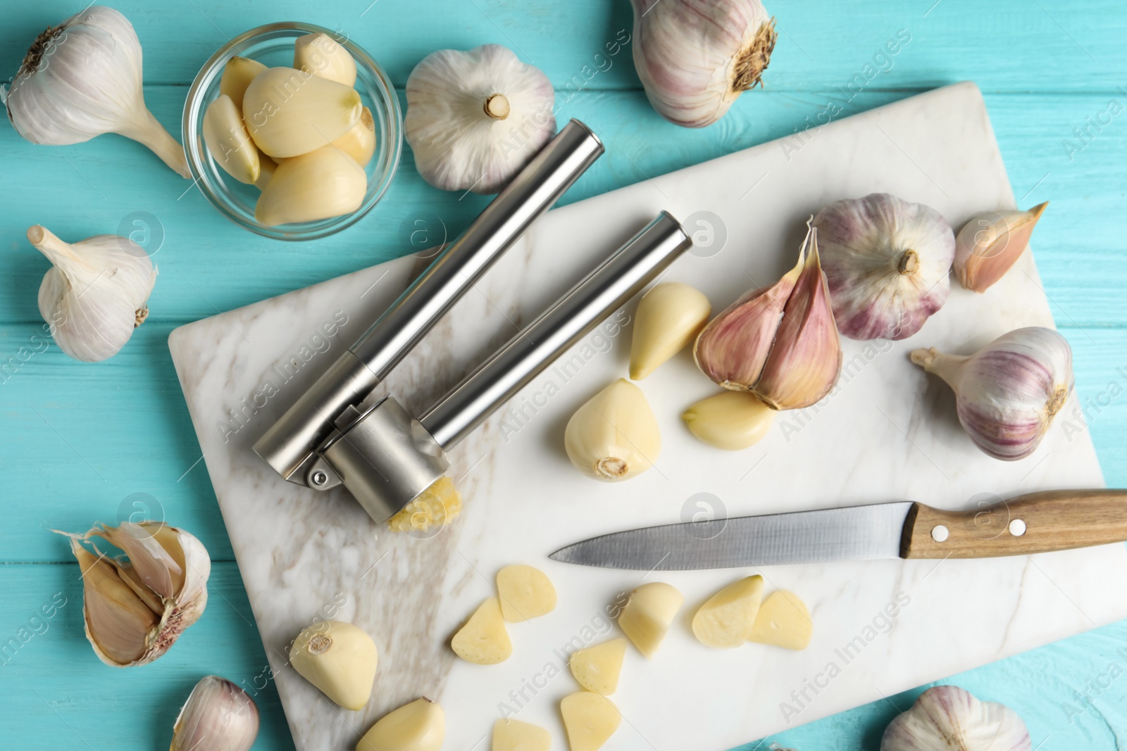 Photo of Flat lay composition with garlic press and fresh cloves on light blue wooden table. Organic product