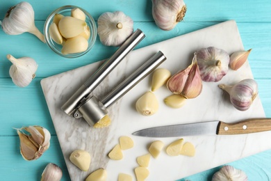 Photo of Flat lay composition with garlic press and fresh cloves on light blue wooden table. Organic product