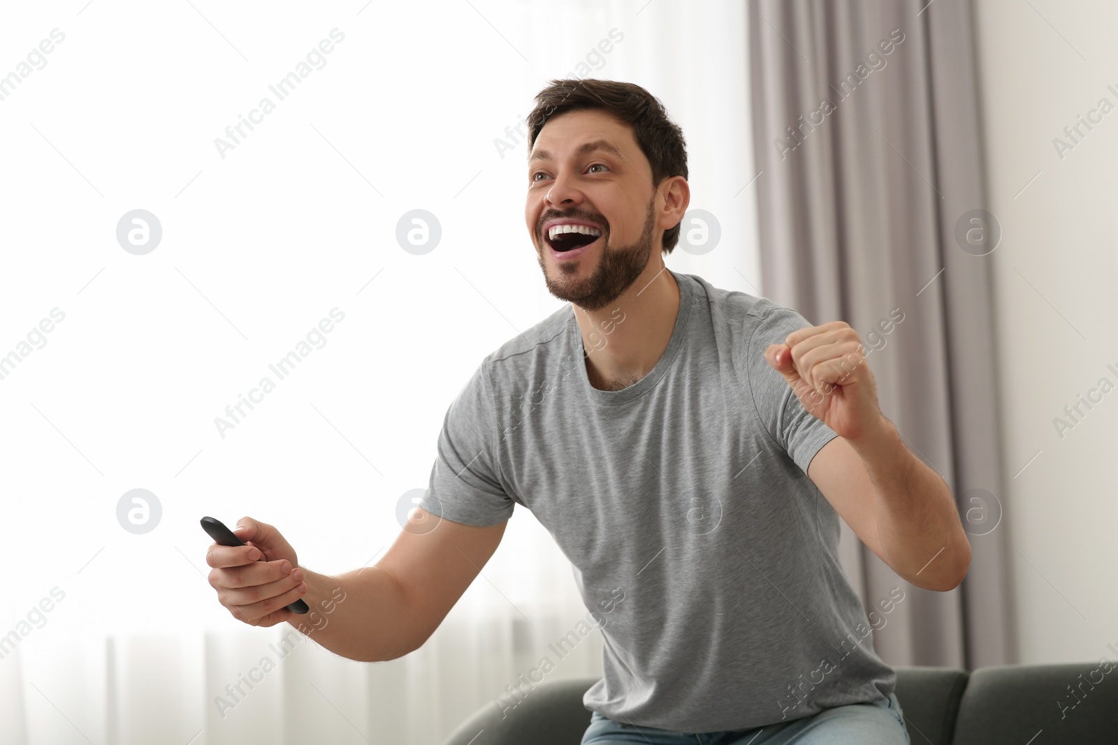 Photo of Emotional man holding remote controller and watching TV at home