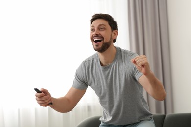 Emotional man holding remote controller and watching TV at home