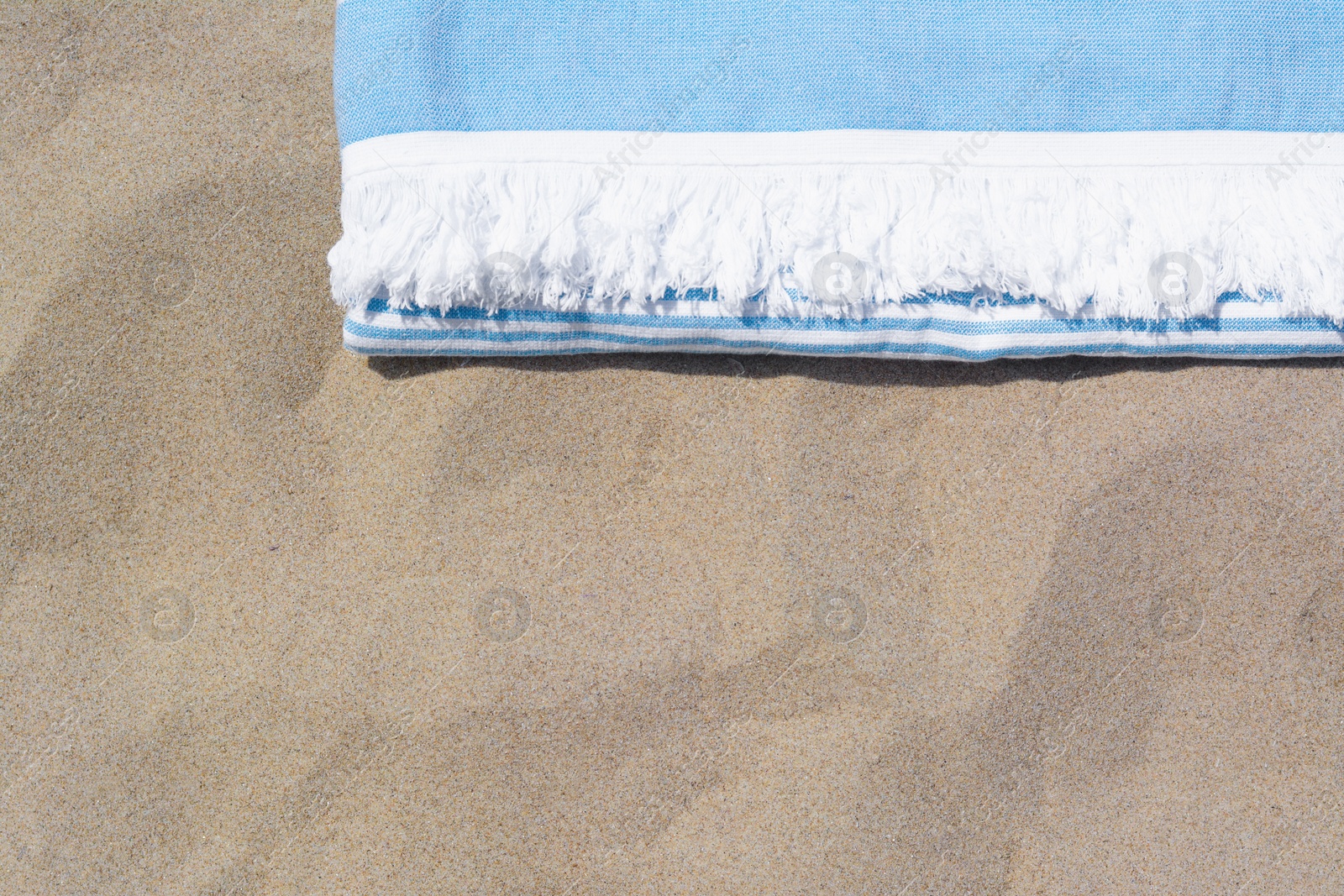 Photo of White and light blue striped towel on sandy beach, top view. Space for text