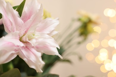 Photo of Beautiful lily flower against beige background with blurred lights, closeup. Space for text