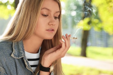 Photo of Young woman smoking cigarette outdoors on sunny day