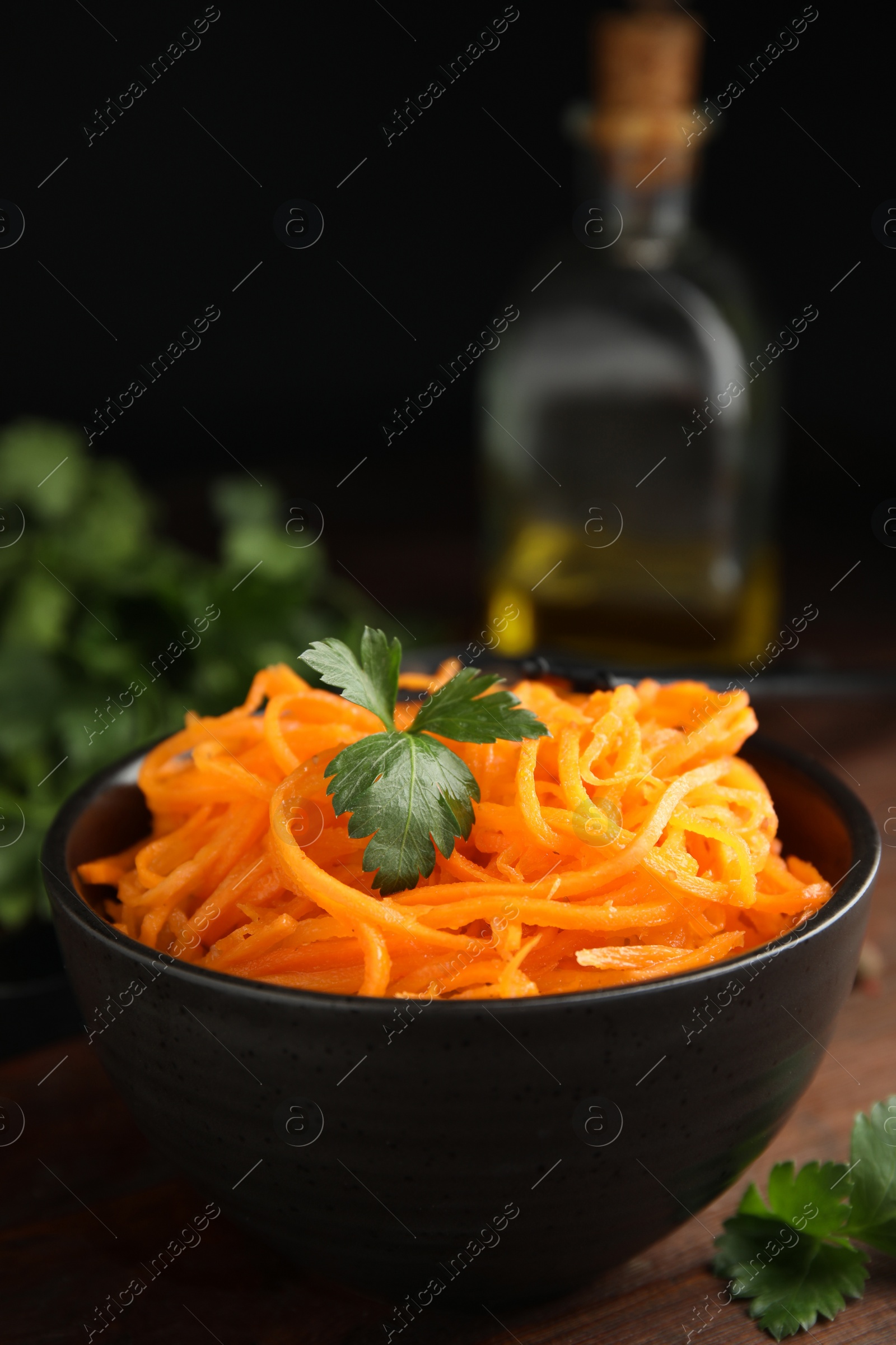 Photo of Delicious Korean carrot salad with parsley in bowl on wooden table