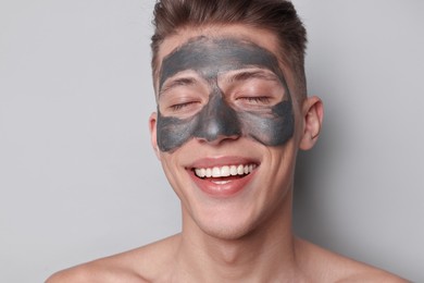 Photo of Handsome man with clay mask on his face against light grey background
