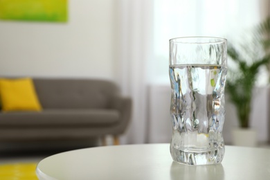 Glass of water on table in room, space for text. Refreshing drink